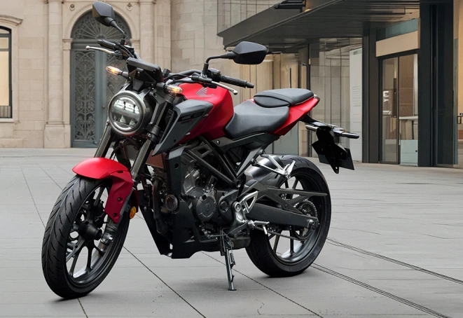 Red Honda CB125R at an angle from the front in front of an urban row of houses – light motorcycle with 11 kW