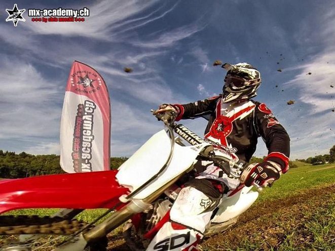 Vale-presente de treino de motocross: piloto numa curva com a bandeira da MX-Academy